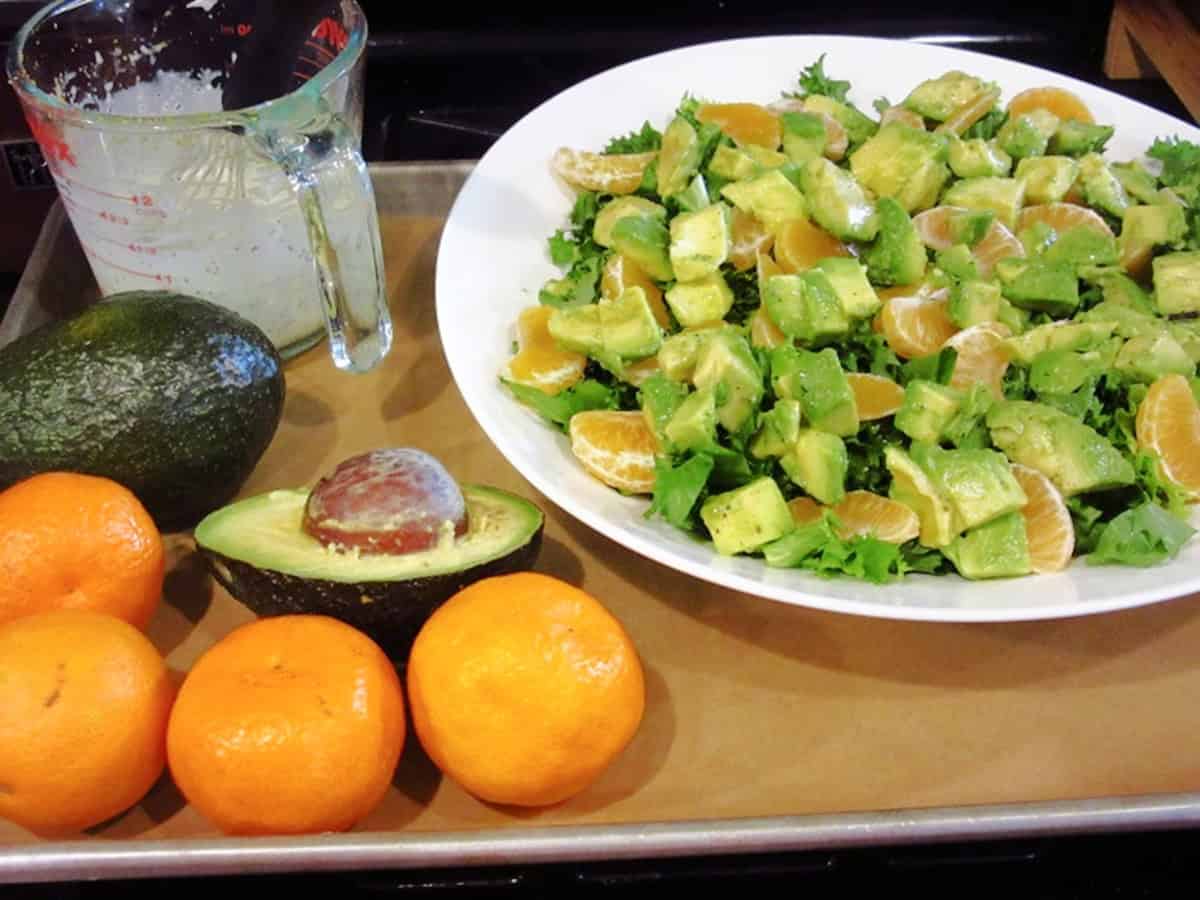 Oranges and avocados on a sheet tray along with the start of a salad with lettuce, avocados, and oranges.