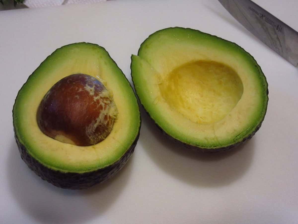A ripe avocado that's been cut in half with the pit still attached.