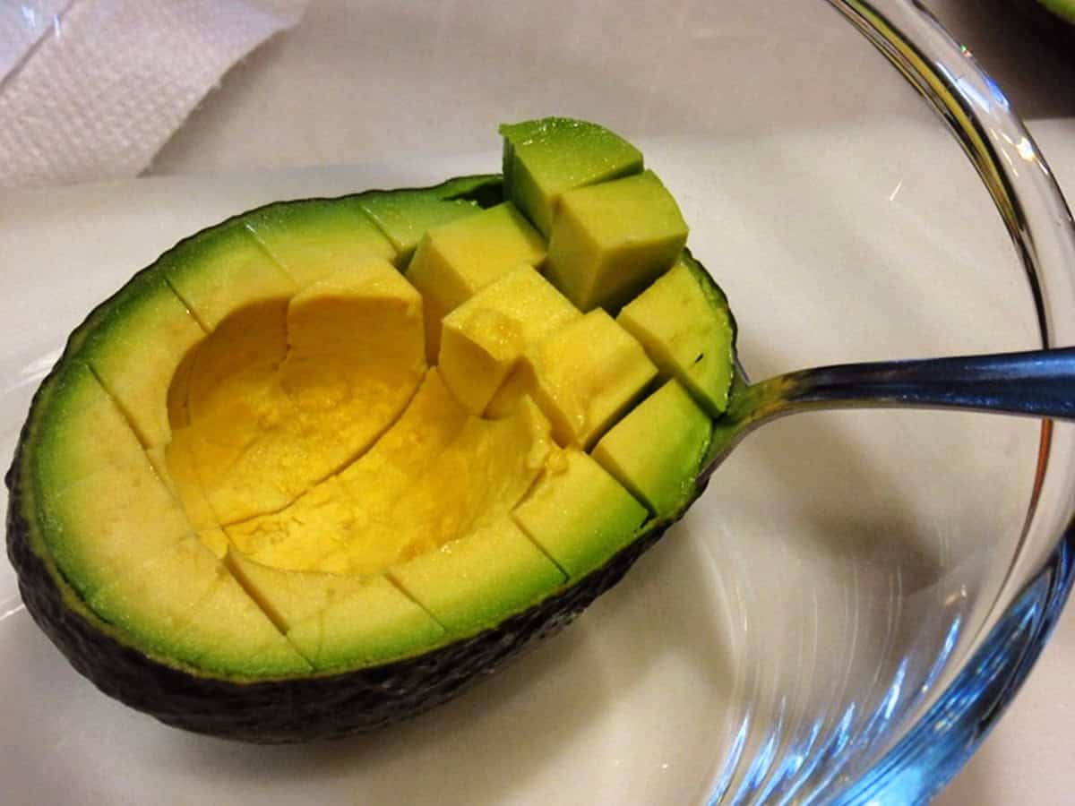 A spoon scooping out the flesh of an avocado after it's been scored.
