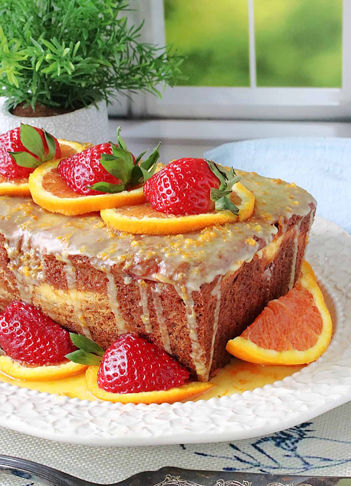 A pretty orange and strawberry glazed loaf cake on a white oval platter.