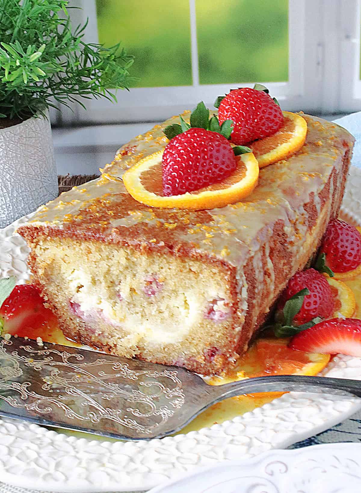 An inside look at an orange strawberry cream loaf cake with orange glaze on top.