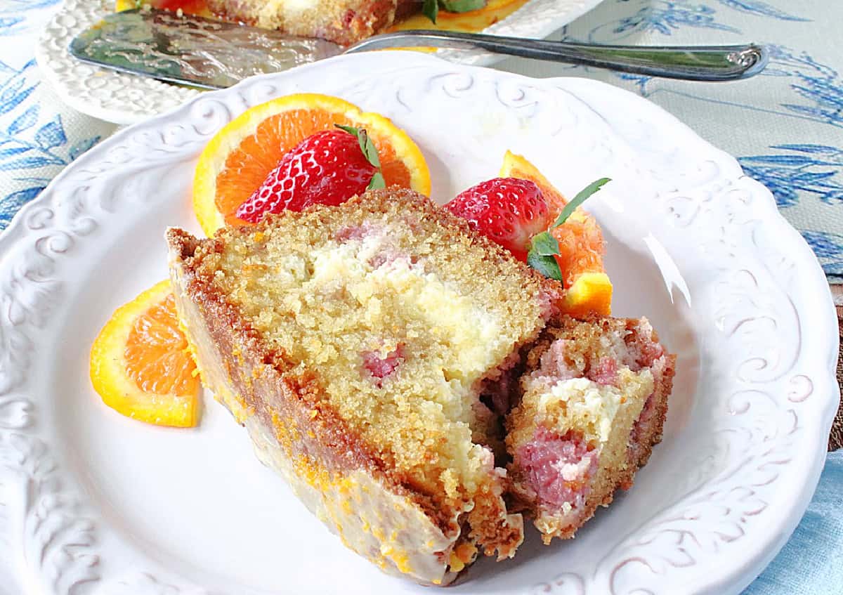 A ribbon of cream cheese running through a slice of orange strawberry loaf cake on a plate.