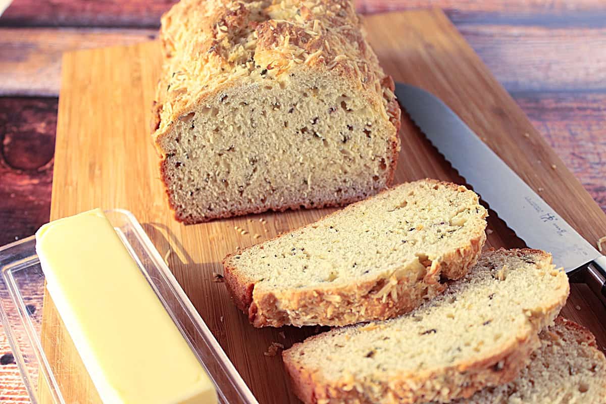 Homemade Soda Bread with Fresh Herbs A loaf of soda bread with fresh herbs on a cutting board with a stick of butter and a serrated knife.