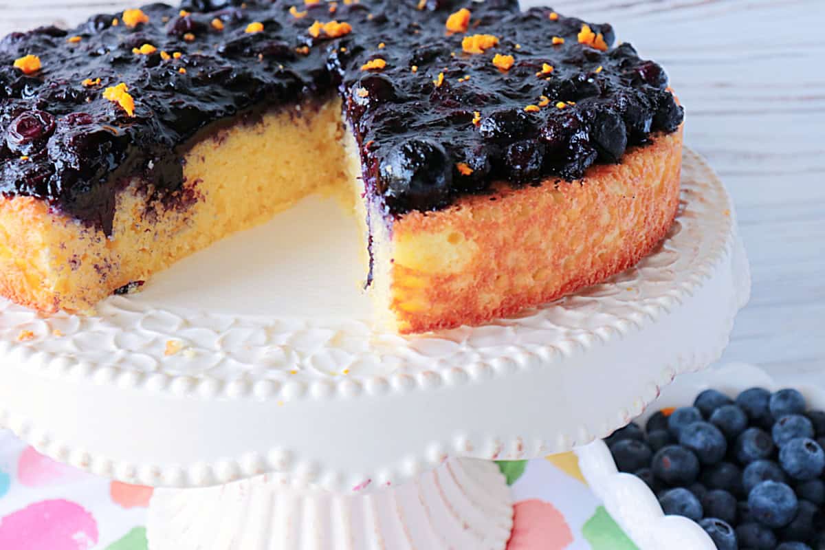 A golden almond cake with a slice taken out on a pretty white cake stand.