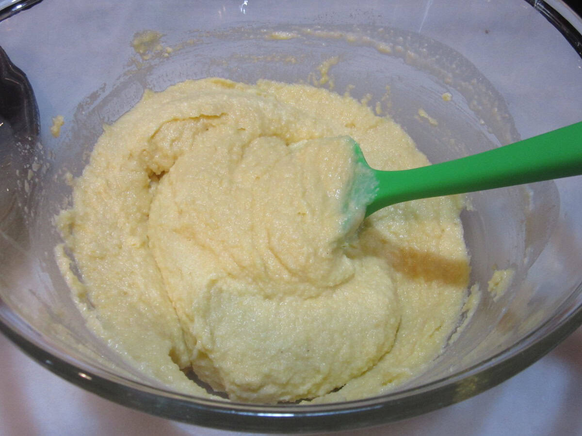 A thick almond cake batter in a glass bowl with a green spatula.