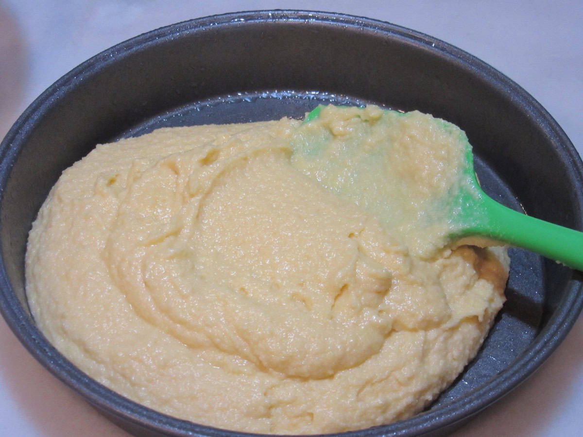 Almond cake batter being added to a round cake pan.