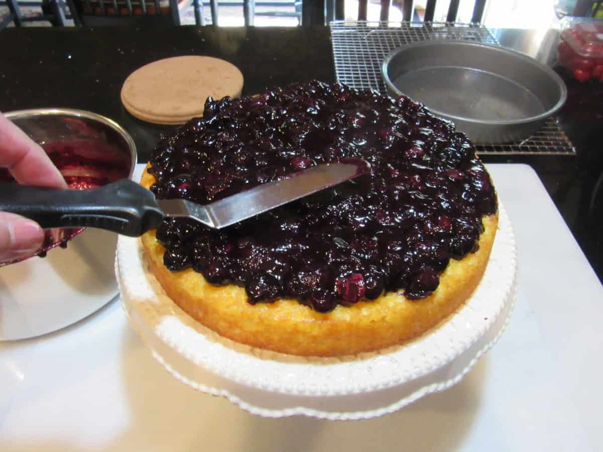 A blueberry and orange compote being added to the top of a baked almond cake.