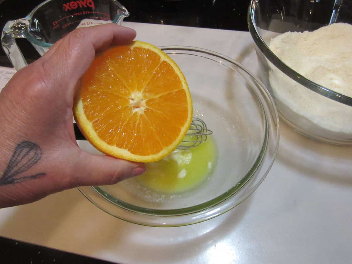 Fresh orange juice being squeezed into a bowl with wet ingredients.