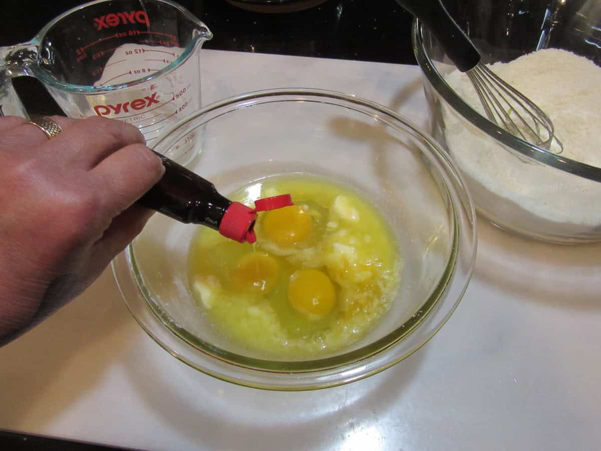 Almond extract being poured into a bowl with eggs and melted butter.