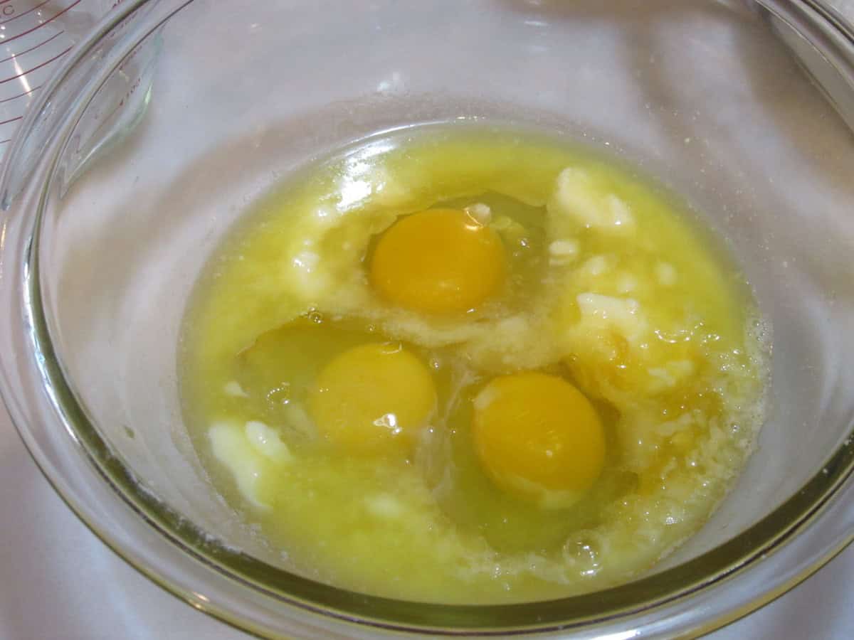 Three eggs and melted butter in a glass bowl.