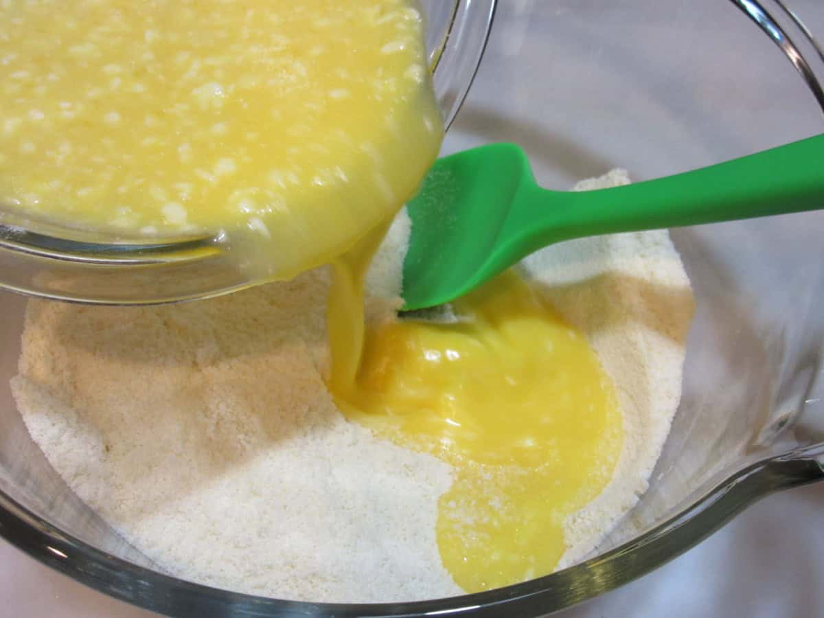 Melted butter being added to almond flour in a glass bowl.