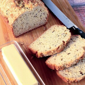 A loaf of golden baked soda bread with fresh herbs on a cutting board.