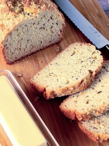 A loaf of golden baked soda bread with fresh herbs on a cutting board.