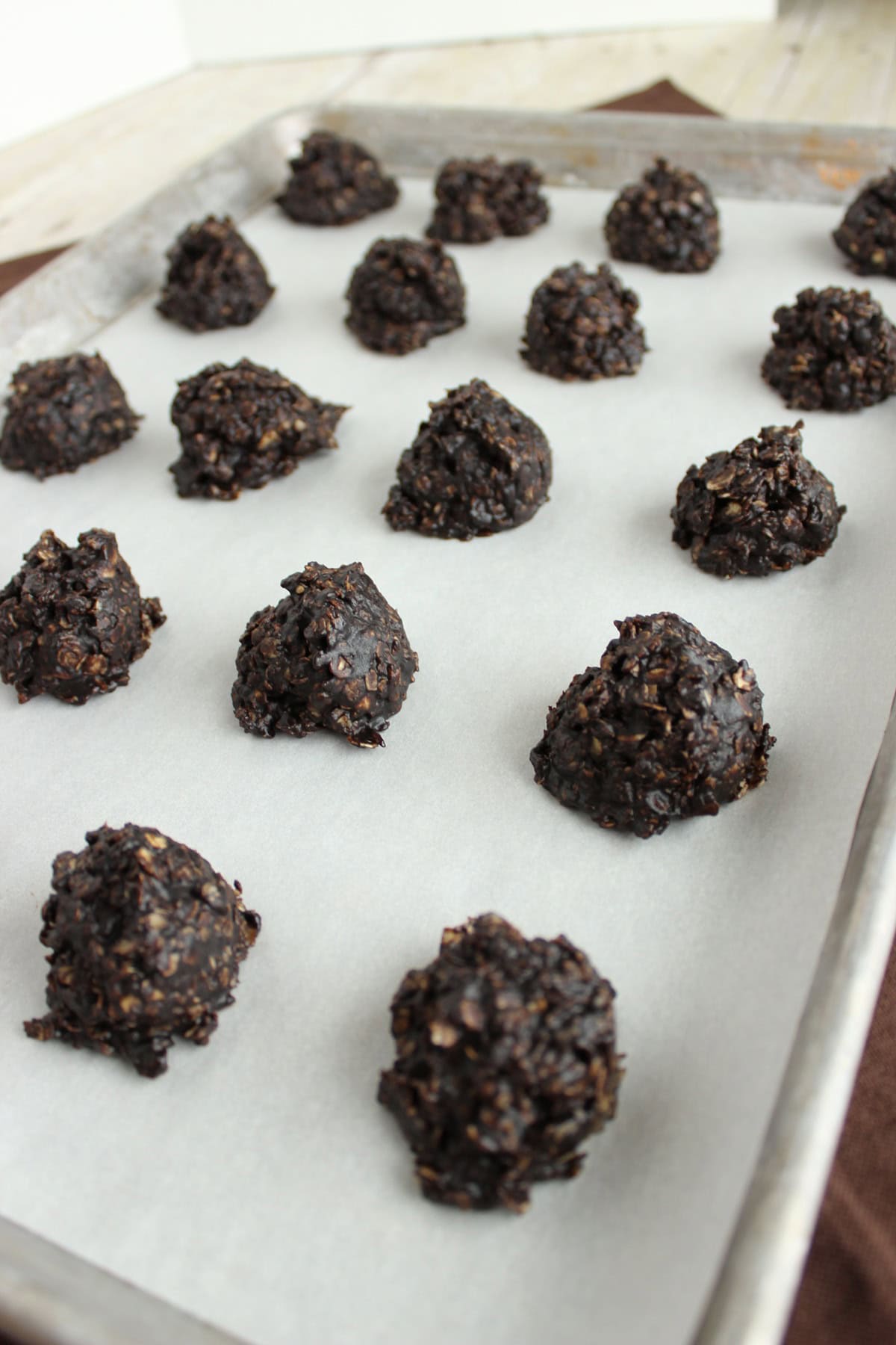Lined up no-bake chocolate drop cookies on a baking sheet with parchment paper.