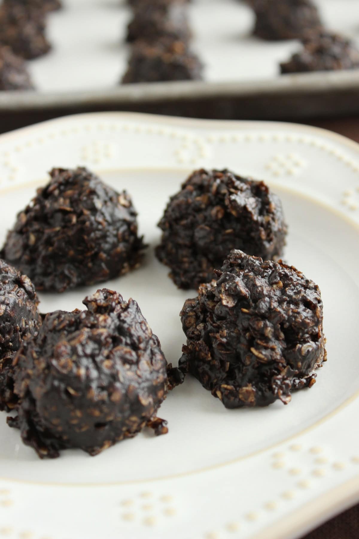 Four delicious looking no bake chocolate and peanut butter drop cookies with oatmeal inside on a white plate.
