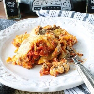 A large serving of cheesy lasagna on a white plate with a fork.