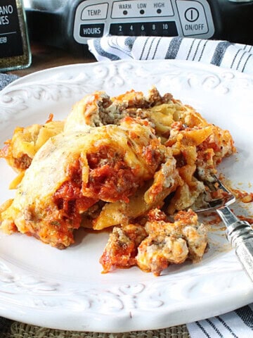 A large serving of cheesy lasagna on a white plate with a fork.