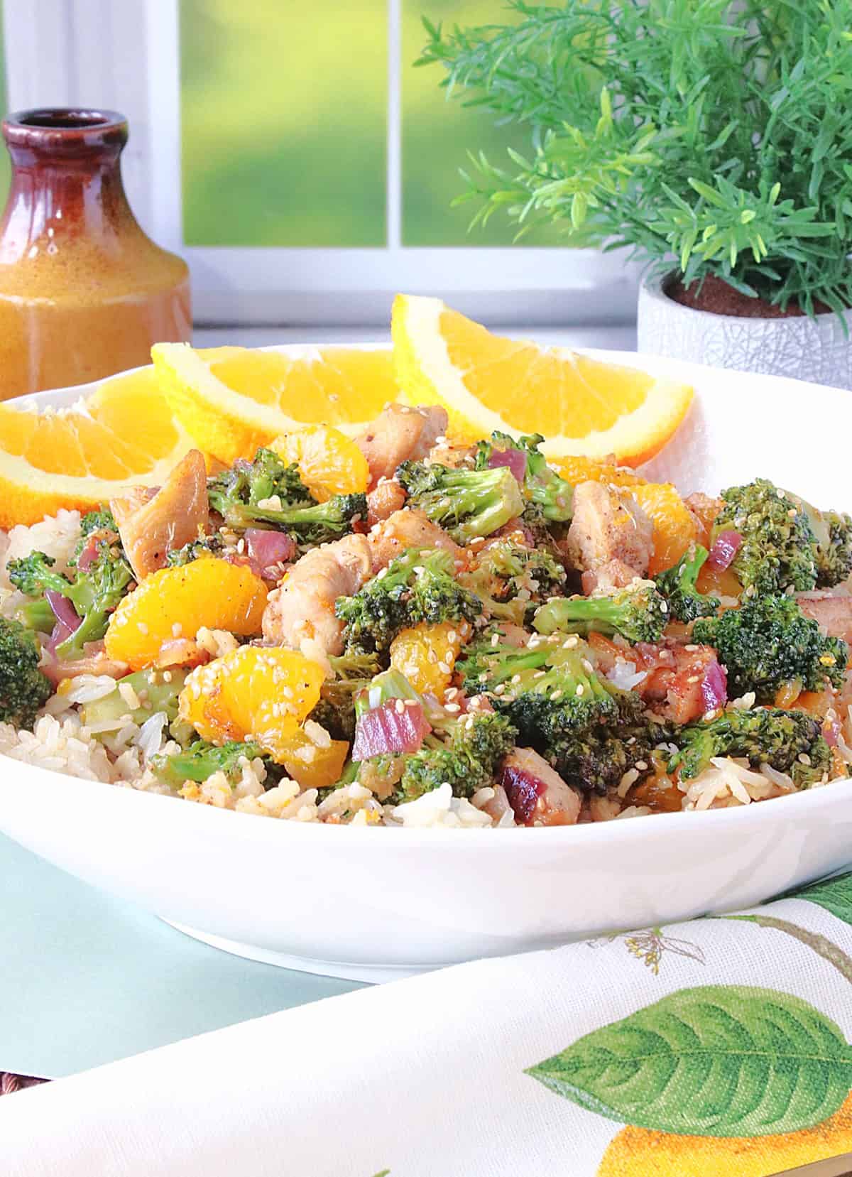 Three orange slices in the bowl along with some rice, chicken, broccoli.
