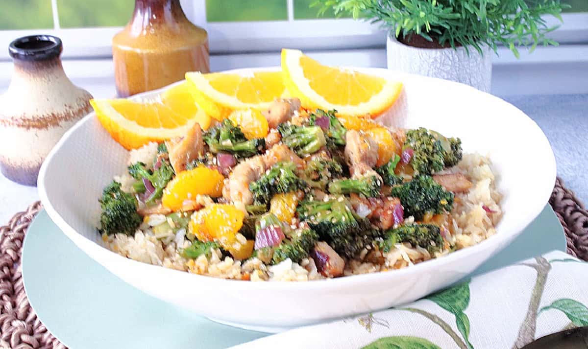 A white bowl filled with chicken, broccoli, onions, and sesame seeds over white rice.