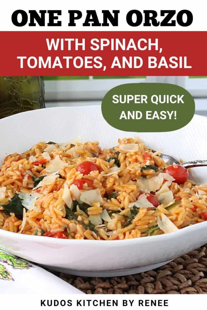 A white bowl filled with cooked orzo pasta, spinach, tomatoes and basil along with a serving spoon.