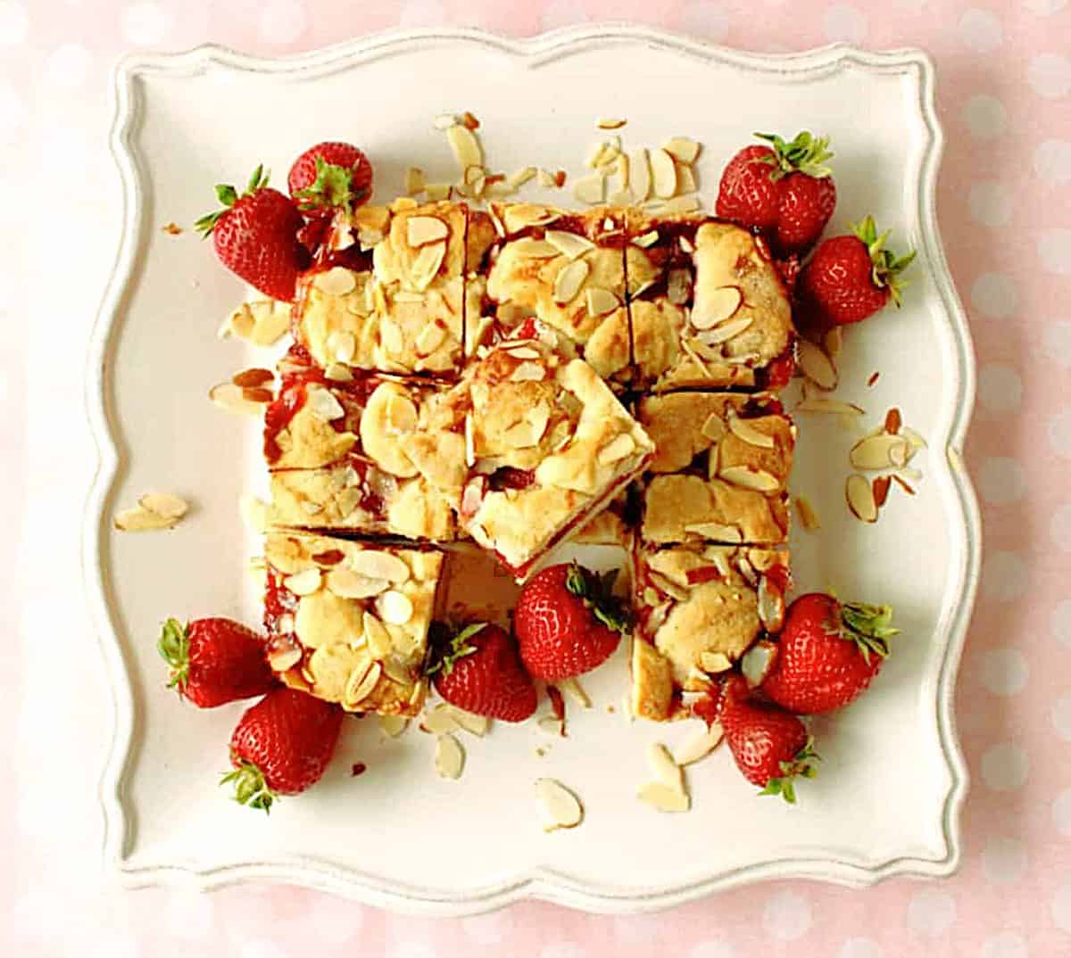 Twelve cut squares of strawberry cobbler bars on a pretty square, white plate.