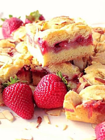 A bunch of cut strawberry cobbler bars stacked on a white plate surrounded by fresh strawberries.