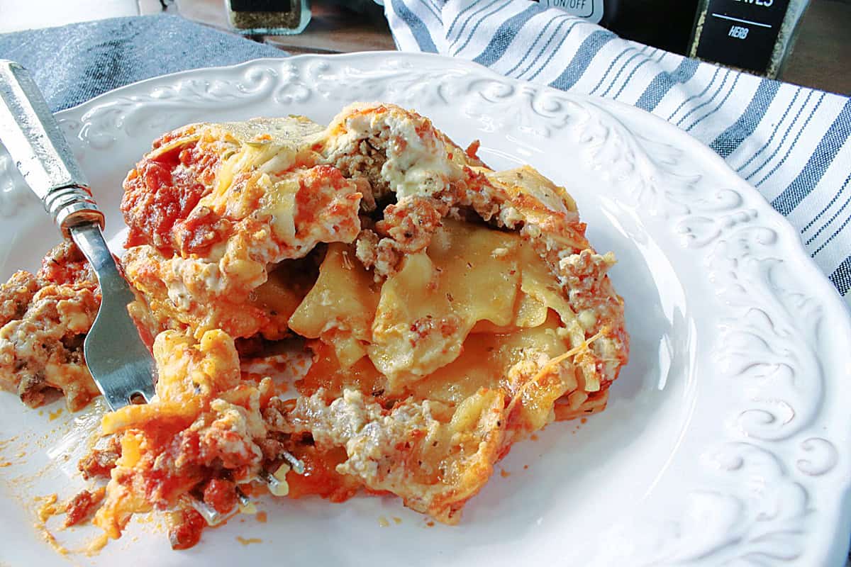 Cooked lasagna with cheese and sausage on a white plate with a fork.