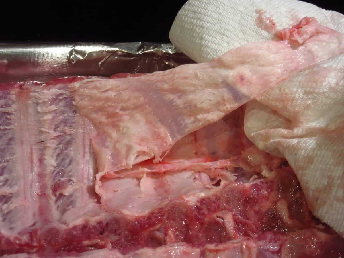 Silver skin from baby back ribs being removed with the help of paper towels.