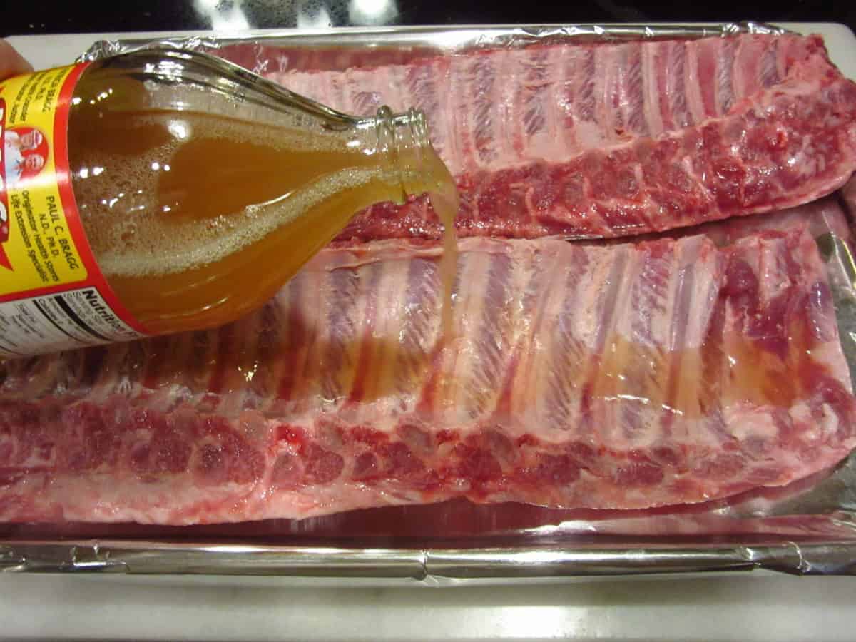 Apple cider vinegar being poured from the jar onto a slab of baby back ribs.