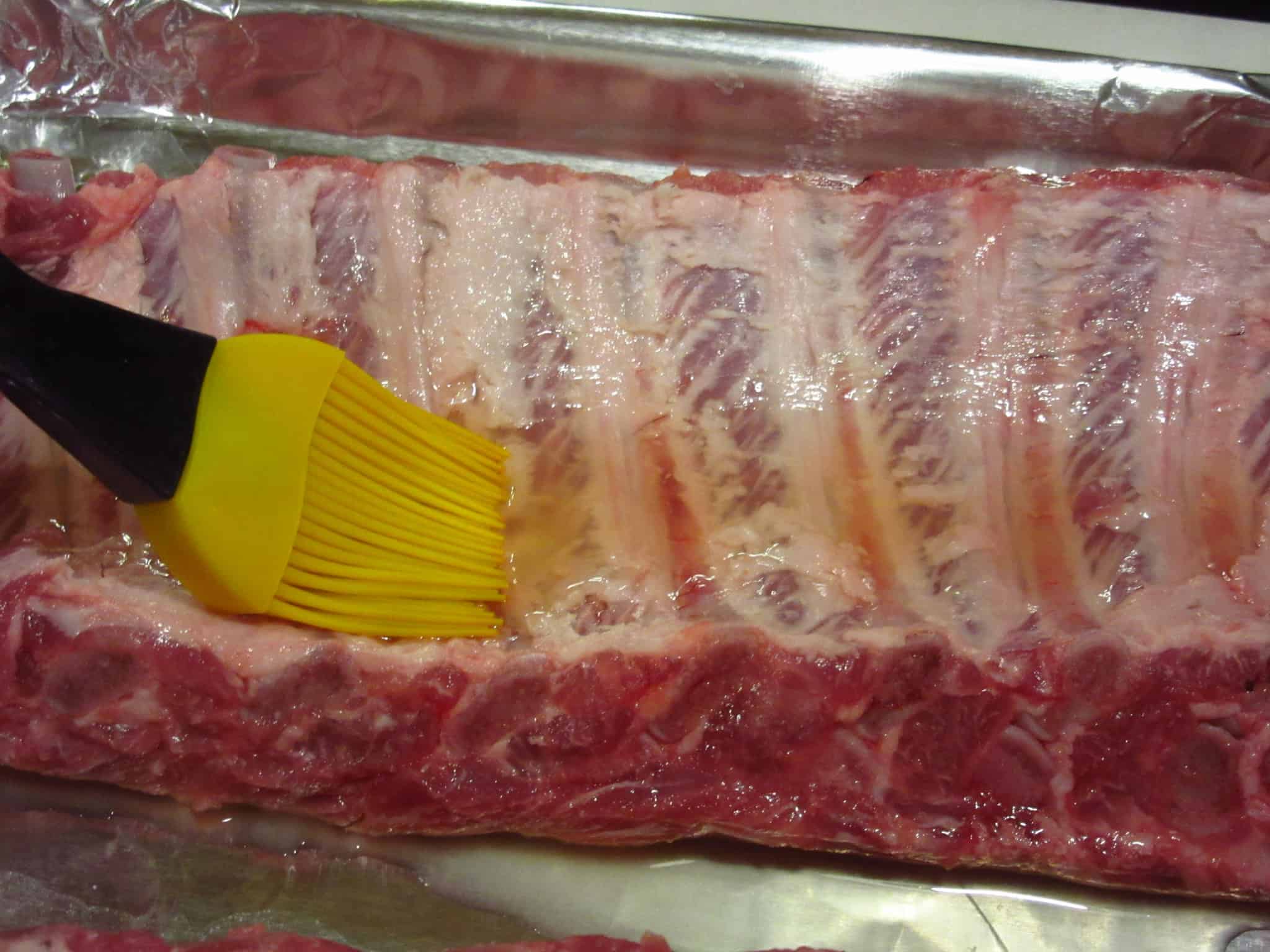 The back side of a slab of ribs being brushed with apple cider vinegar.