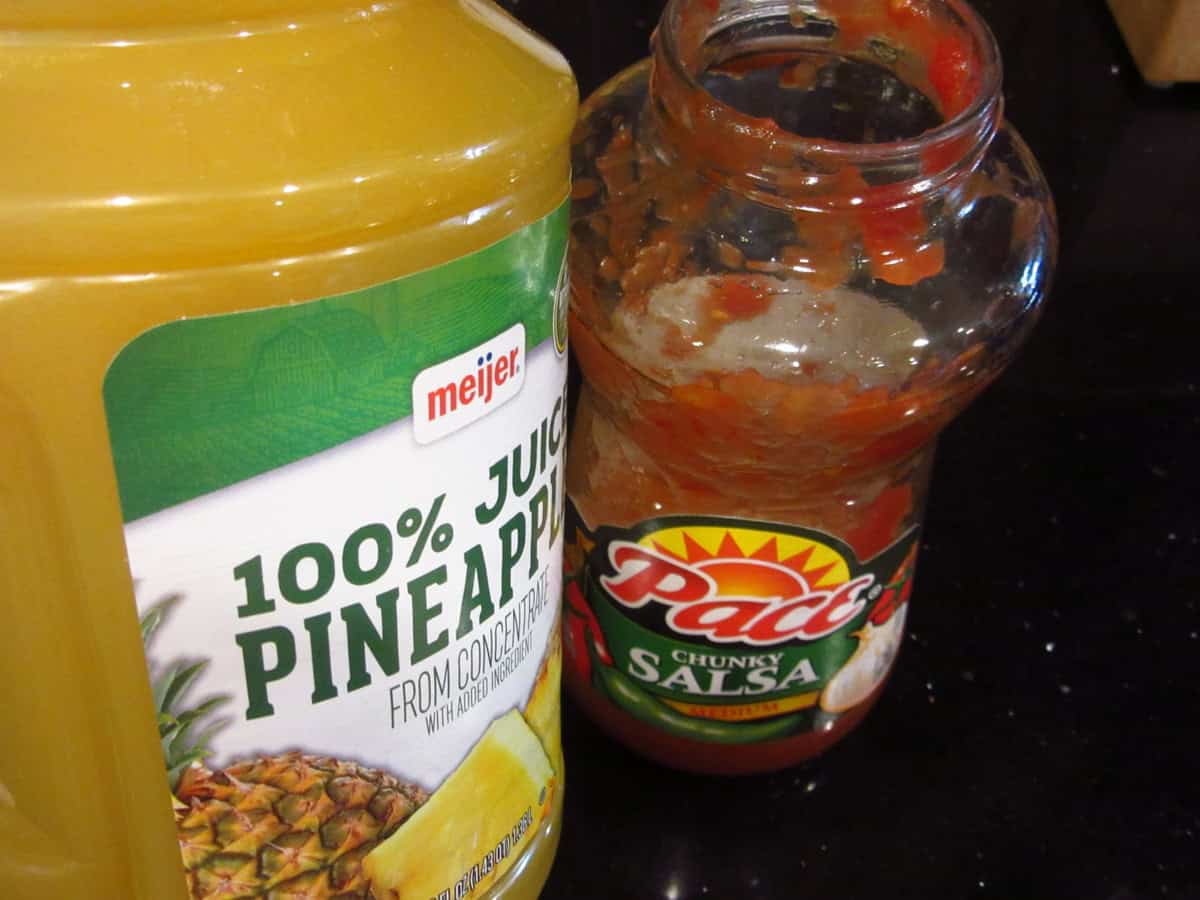 A jug of pineapple juice and a half empty jar of salsa on the counter.