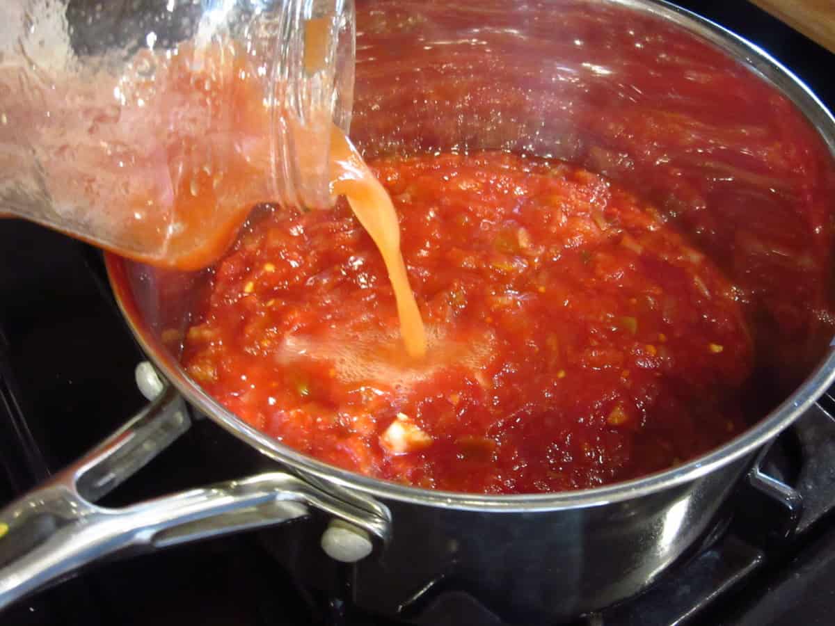 Pineapple juice being poured into a saucepan of salsa BBQ sauce on the stovetop.