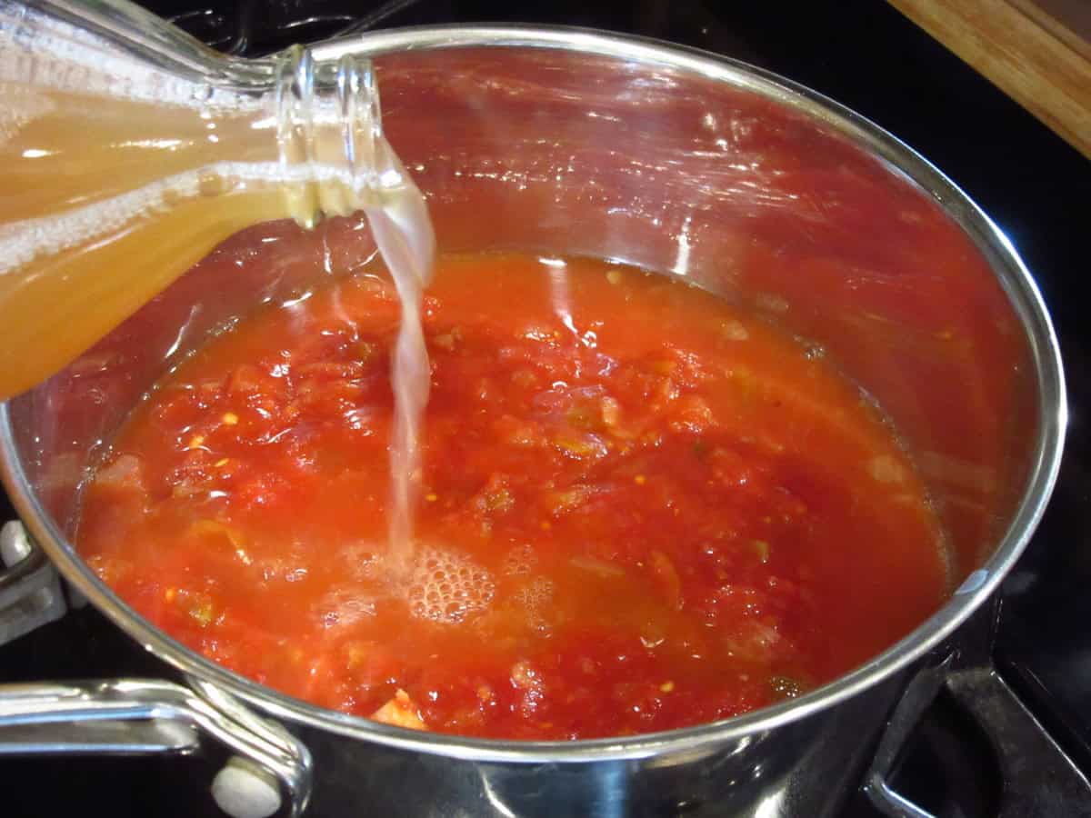 Apple cider vinegar being poured into a saucepan of salsa BBQ sauce on the stovetop.