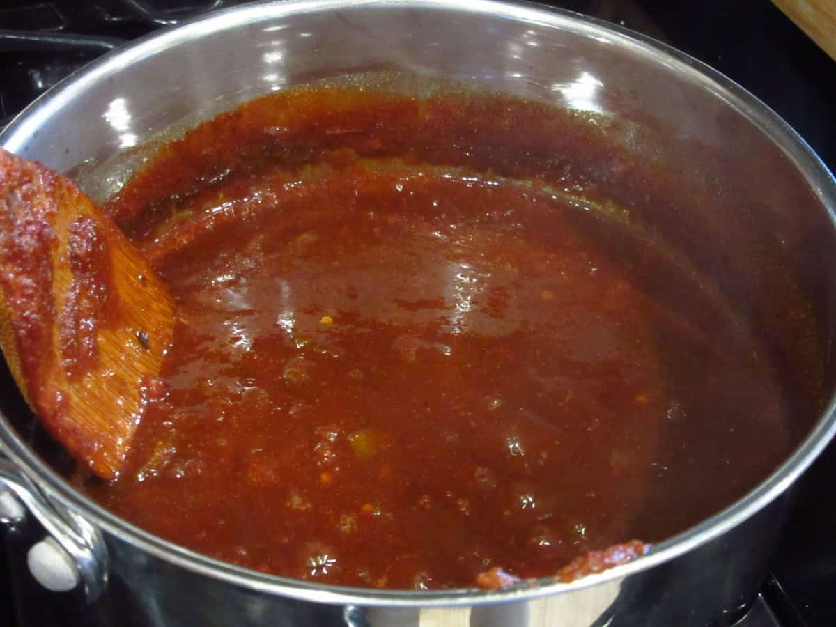 A wooden spoon stirring BBQ salsa sauce in a saucepan on the stovetop.