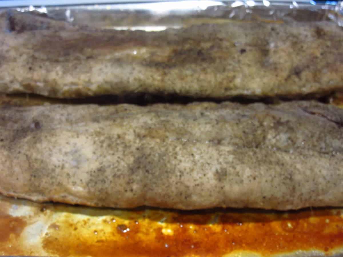Two slabs of partially cooked baby back ribs on a baking sheet.