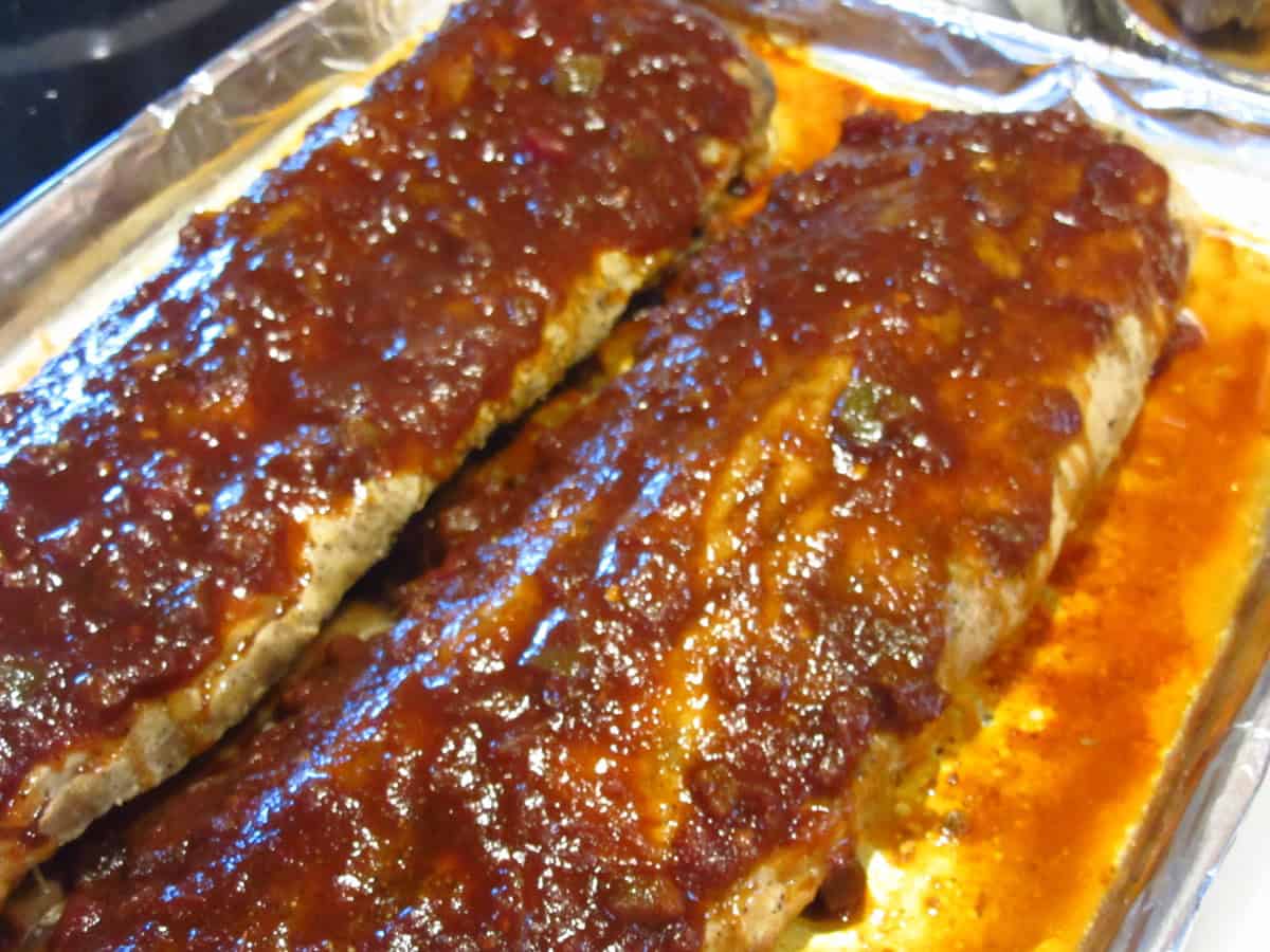 A tin foil covered baking sheet with two slabs of salsa BBA sauce topped baby back ribs on top.