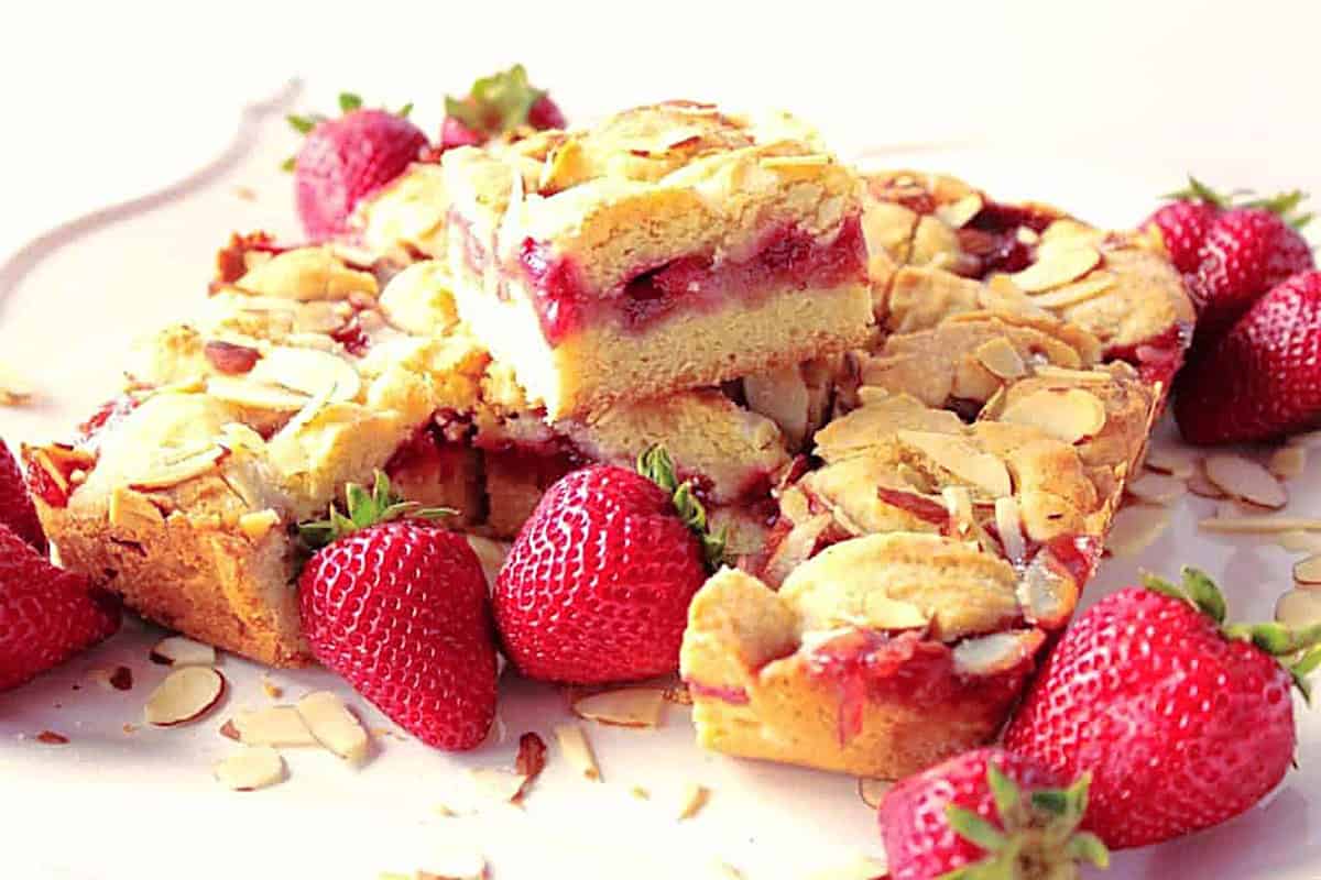 Delicious looking layered strawberry cobbler bars on a platter with strawberries and almond slices.