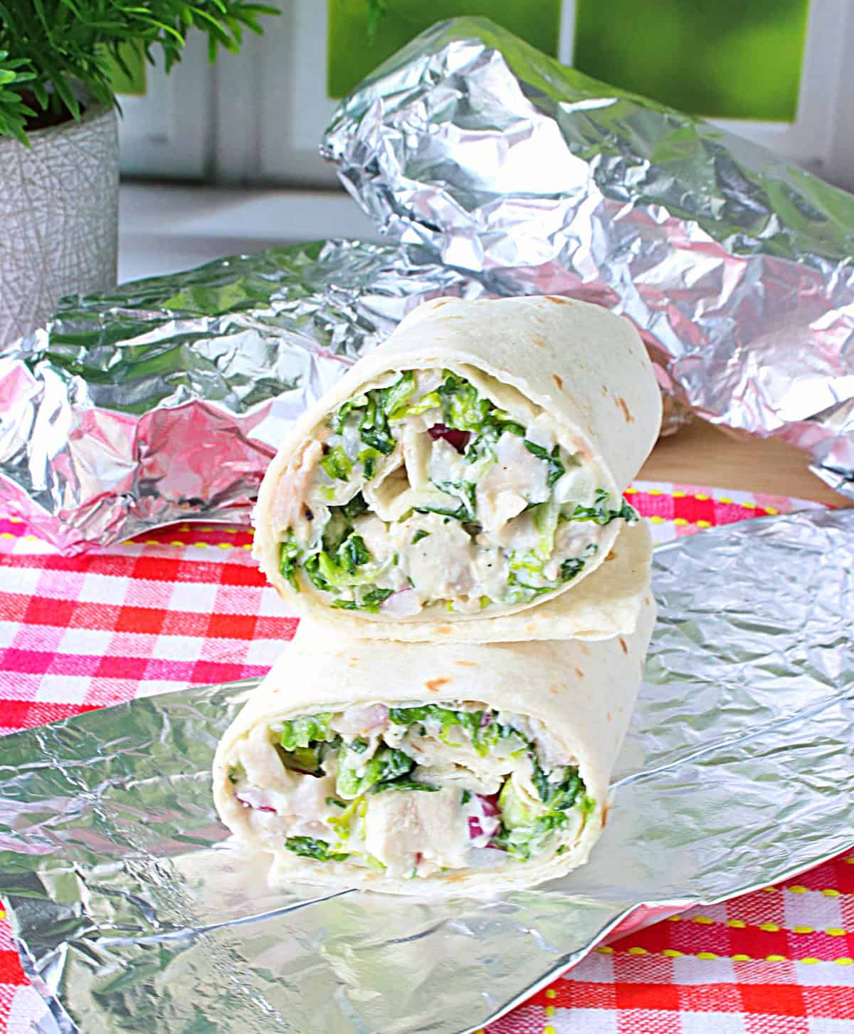 A cut in half chicken Caesar salad wrap filled with lettuce, chicken and dressing on a sheet of foil.