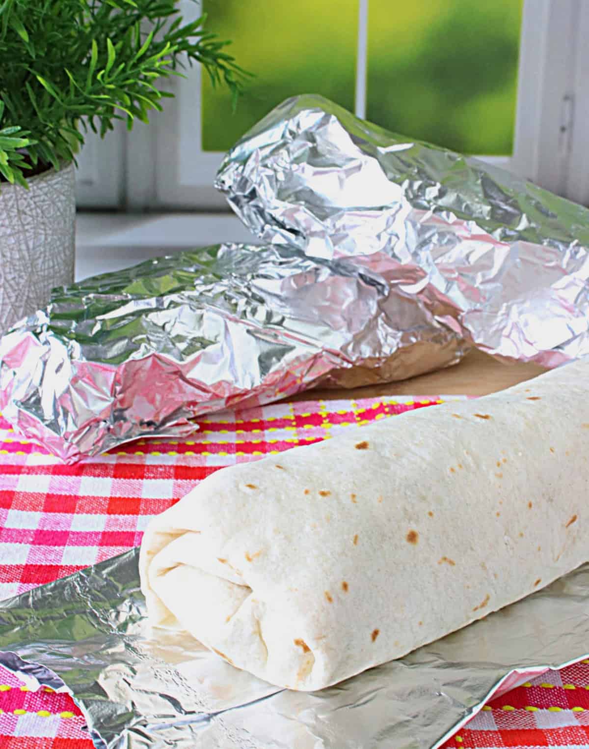 A chicken Caesar salad wrap in a flour tortilla on a sheet of foil.