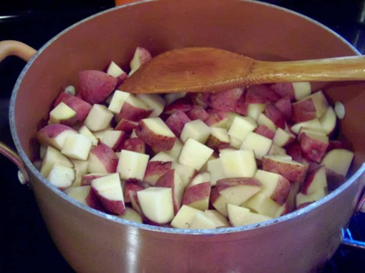 Diced red potatoes in a stockpot with a wooden spoon.