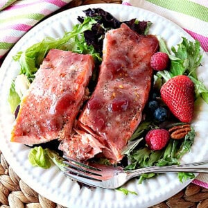 Two salmon fillets glazed with strawberry jam on a white plate with lettuce, berries and a fork.