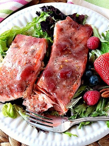 Two salmon fillets glazed with strawberry jam on a white plate with lettuce, berries and a fork.