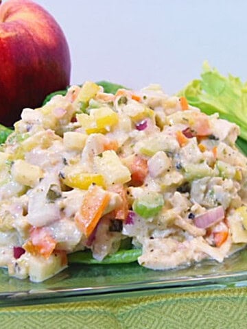 A red apple and rib of celery next to a glass plate with a serving of rainbow chicken salad on top.