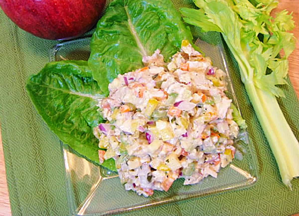 A glass plate with two large lettuce leaves and a mound of homemade rainbow chicken salad sitting on top.