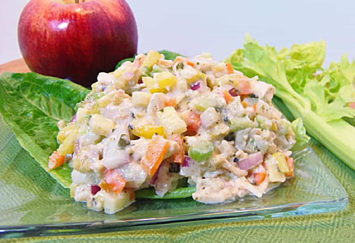 A square glass plate with a mound of colorful rainbow chicken salad on top with colorful bell peppers, onions, and celery.