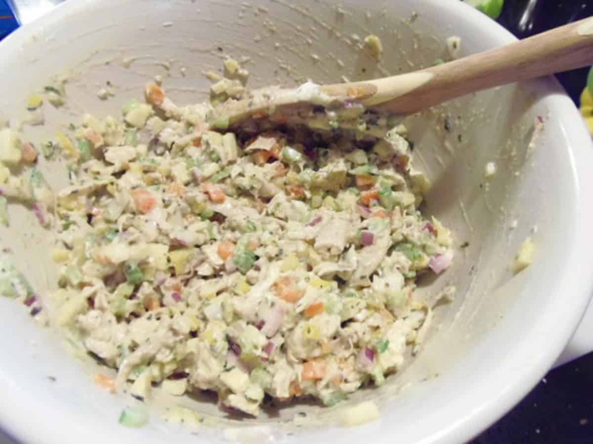 A wooden spoon inside a big bowl of freshly mixed homemade rainbow chicken salad.