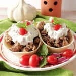 Two fillable tortilla bowls on a plate with cooked, ground lamb and topped with homemade tzatziki sauce.