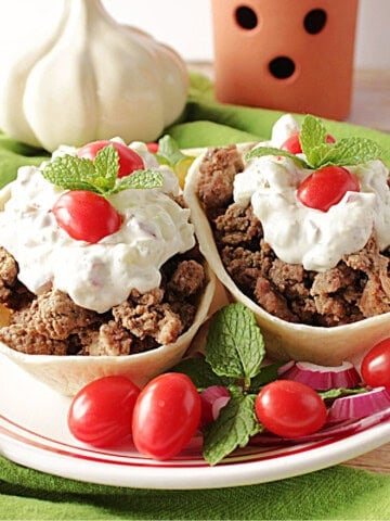 Two fillable tortilla bowls on a plate with cooked, ground lamb and topped with homemade tzatziki sauce.