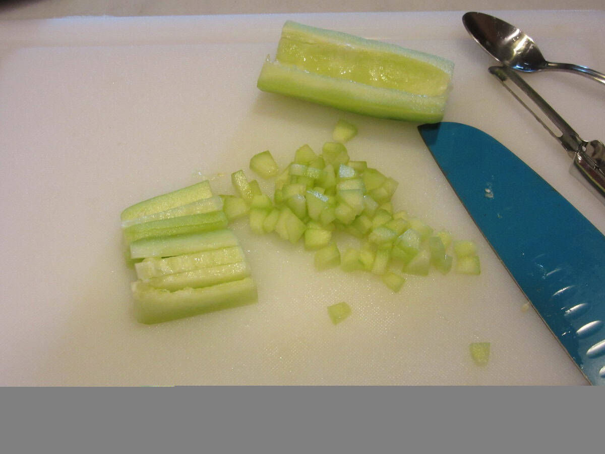 A seeded and dices cucumber on a white cutting board with a blue knife.
