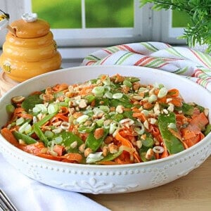 Orange shredded carrots and green snow peas mixed together in a white bowl.